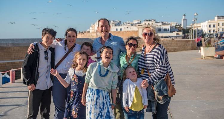 Una familia grande y sonriente posando en un paseo marítimo con los muros blancos de Essaouira de fondo.