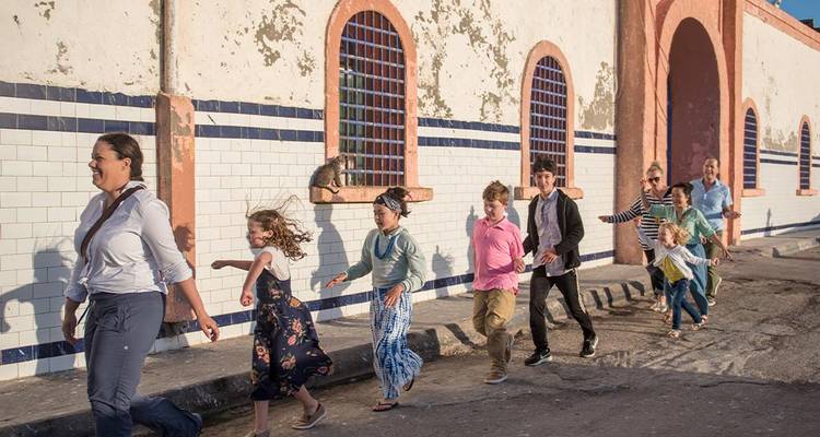 Una familia caminando juguetonamente por una pared de azulejos iluminada por el sol con pintura desconchada y ventanas arqueadas.