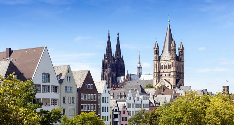 Les anciennes maisons du centre-ville de Cologne avec les flèches de la cathédrale s'élevant derrière sur un ciel bleu dégagé.
