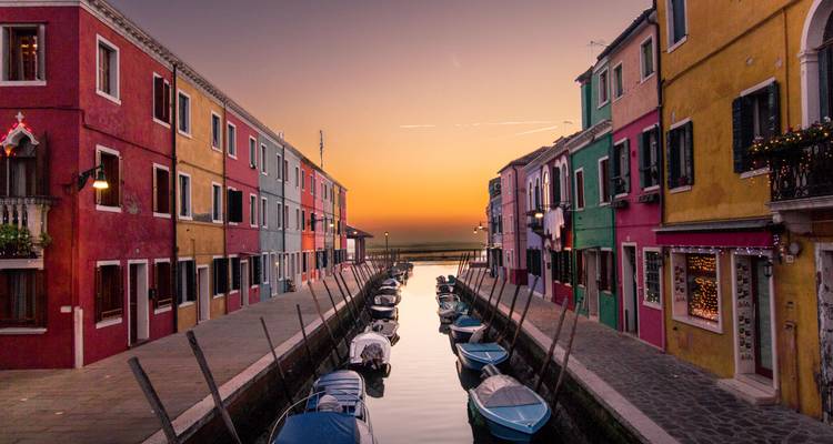 Quiet canal between colorful houses at sunset with boats gently moored along Burano.