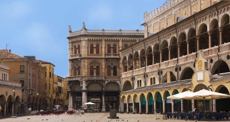 Historic arcaded market buildings and outdoor cafés bordering a sunny Italian piazza.