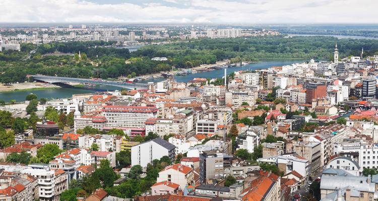 Vista aérea expansiva de Belgrado que muestra la confluencia de dos ríos, puentes y la densa trama urbana.
