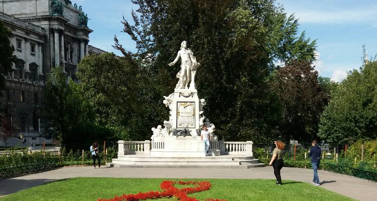 Statue of Mozart stands in Vienna’s Burggarten surrounded by manicured flower beds and visitors.