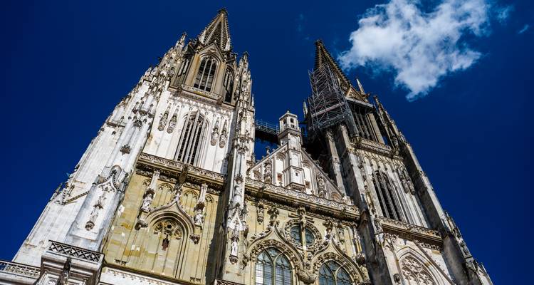 Upward view of twin spires and ornate façade of Gothic cathedral against deep blue sky.