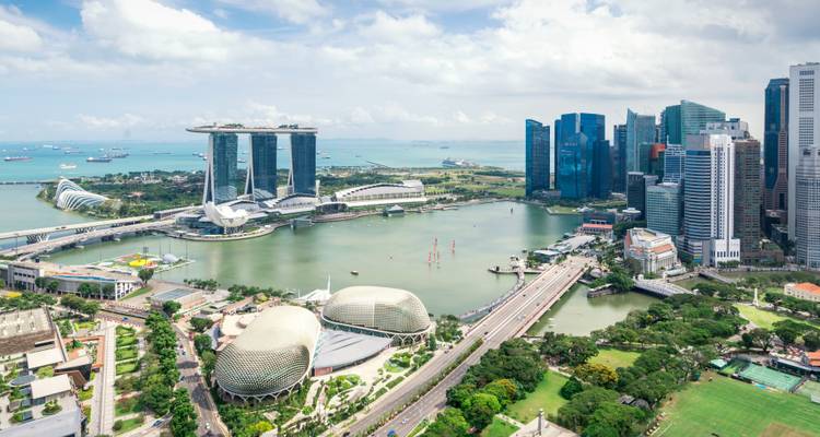 Aerial panorama of Singapore's Marina Bay with Marina Bay Sands, the Esplanade domes and modern skyscrapers beside a blue harbor.