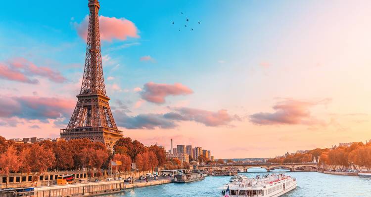 La Tour Eiffel s'élevant au-dessus des arbres aux couleurs automnales avec un bateau de croisière sur la Seine au coucher du soleil.