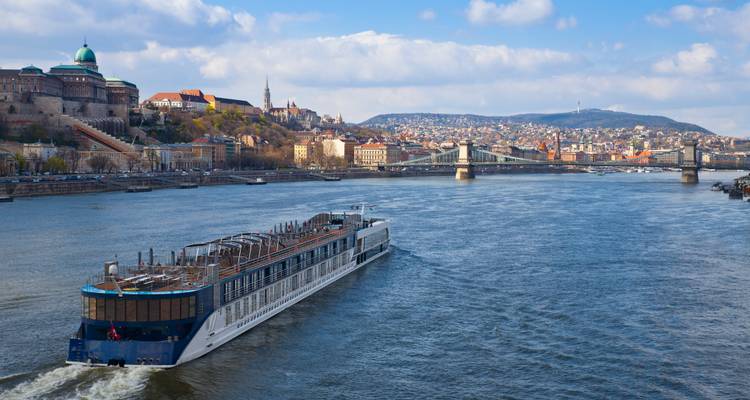 Un navire de croisière fluviale remonte le Danube, laissant derrière lui les ponts de Budapest et le quartier du château sous des cieux brumeux.