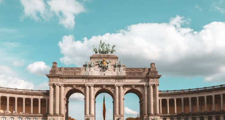 Arco del Cincuentenario triunfal en Bruselas enmarcado por cielo azul y nubes blancas.