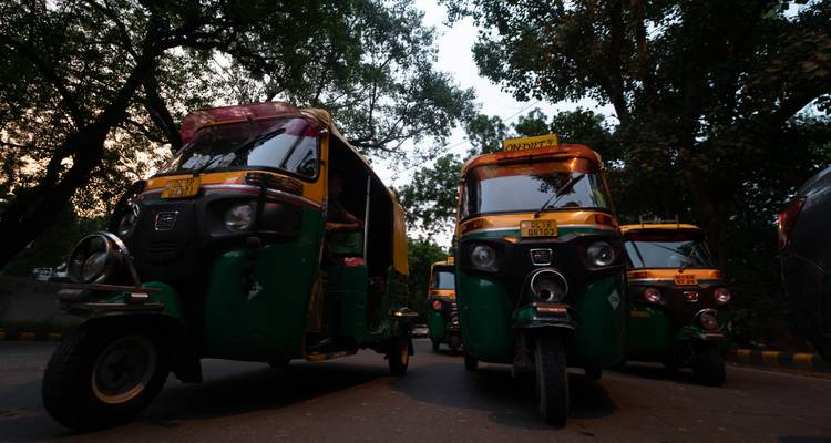 Scène faiblement éclairée d'auto-rickshaws dans une rue bordée d'arbres en soirée.