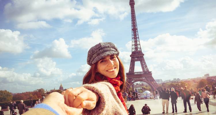 Joven mujer tomada de la mano de su pareja frente a la Torre Eiffel en un día soleado.