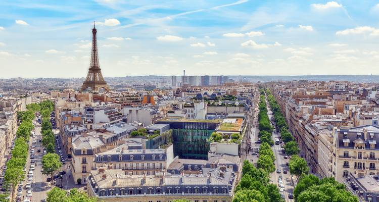 Vista aérea expansiva de los bulevares de París con la Torre Eiffel elevándose en el horizonte.