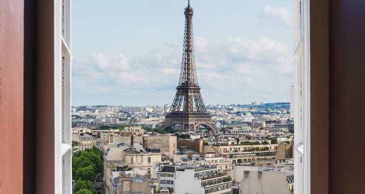 Vista de la Torre Eiffel enmarcada por una ventana abierta con vistas a los tejados de París.