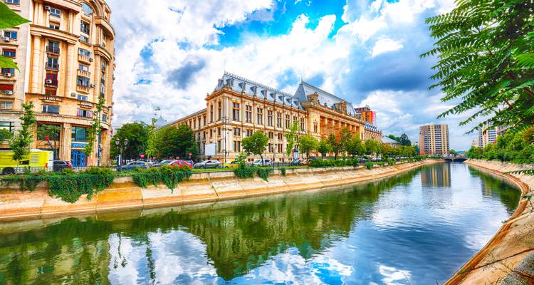 Vue pittoresque de bâtiments historiques élégants longeant un canal avec des reflets vibrants sous un ciel bleu partiellement nuageux.