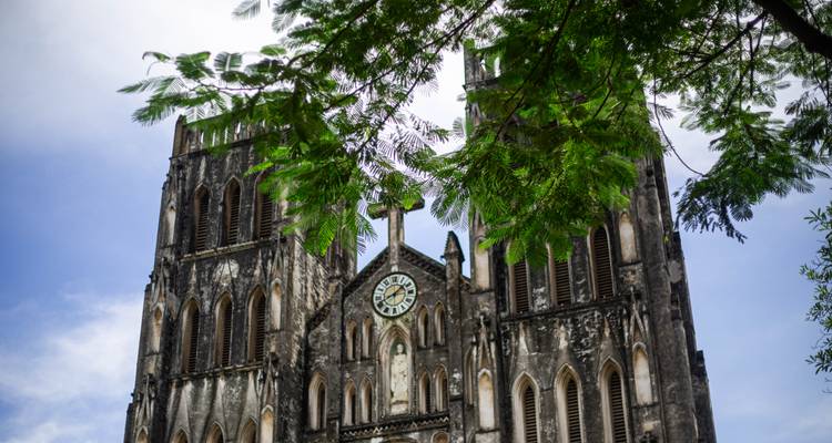 Les deux tours de la Cathédrale Saint-Joseph à Hanoï vues à travers les branches feuillues sous un ciel dégagé.