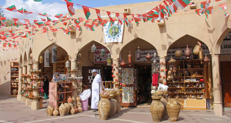 Souk omanais traditionnel avec poterie, artisanat et guirlandes colorées au-dessus.