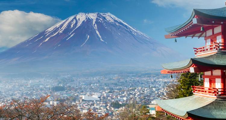 Mount Fuji rises majestically behind the red Chureito Pagoda overlooking the city and autumn trees.