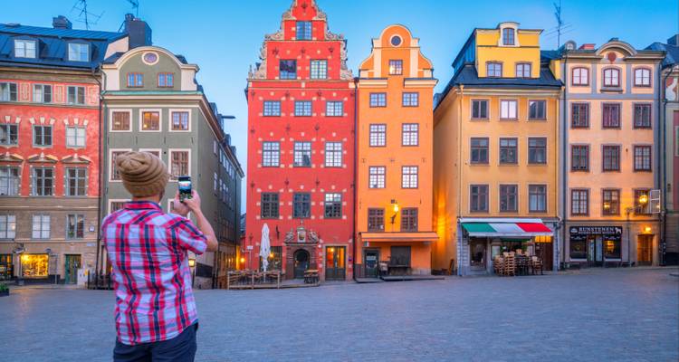 Un voyageur photographiant des maisons de ville colorées dans une place vide en début de matinée à Stockholm.