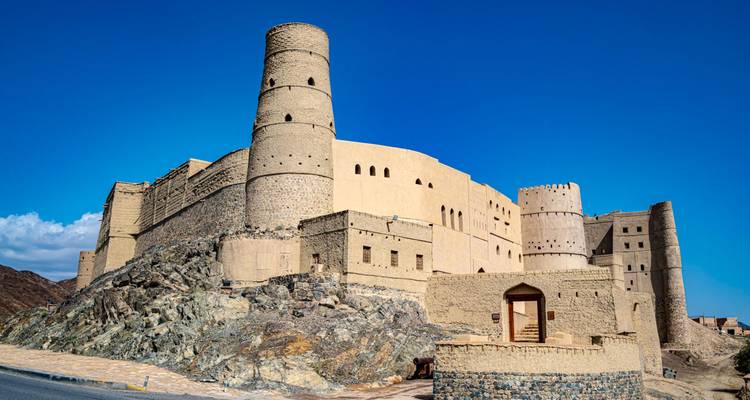 Les imposants murs en pierre et les tours cylindriques du fort de Bahla se dressent contre un ciel bleu profond.