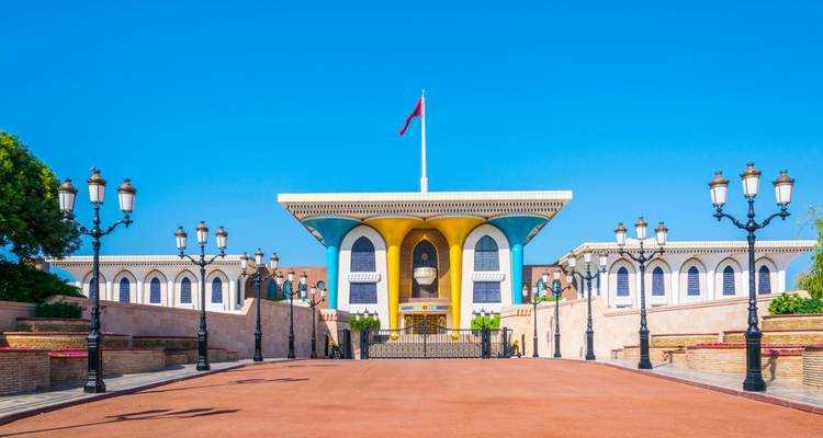Le Palais royal Al Alam à Mascate avec façade colorée et mât de drapeau centré sous un ciel dégagé.