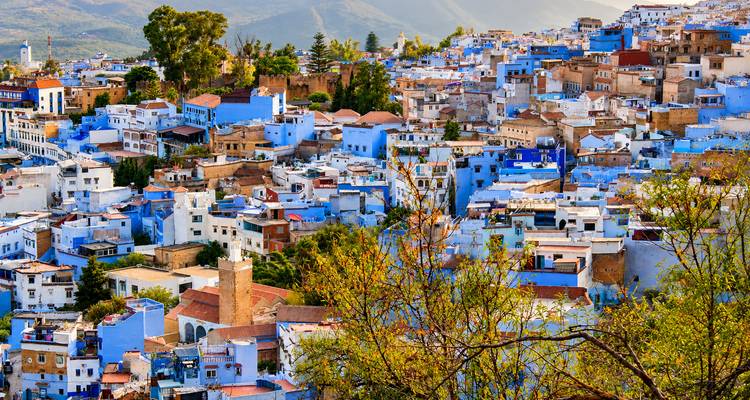 Una vista más cercana del paisaje urbano de Chefchaouen con sus edificios azules y tonos tierra, con las colinas al fondo.