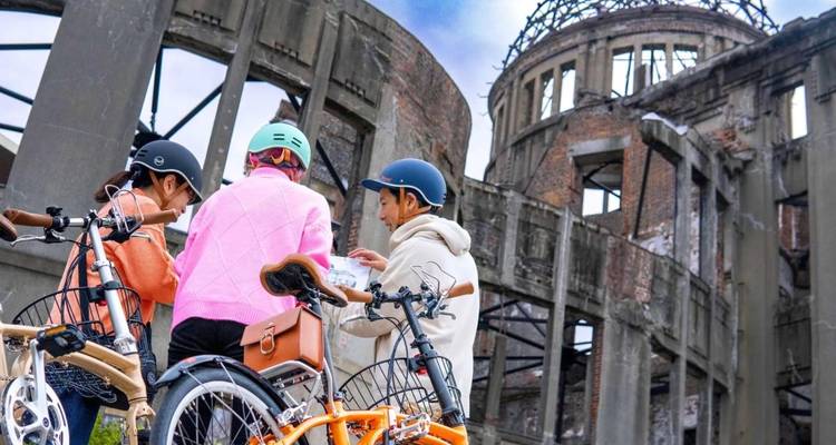 Radfahrer konsultieren eine Karte neben dem ikonischen zerstörten Atomkuppel-Gebäude in Hiroshima.