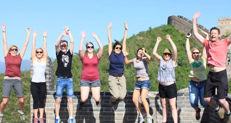 Group of travellers jumping joyfully on a section of the Great Wall with green hills behind.