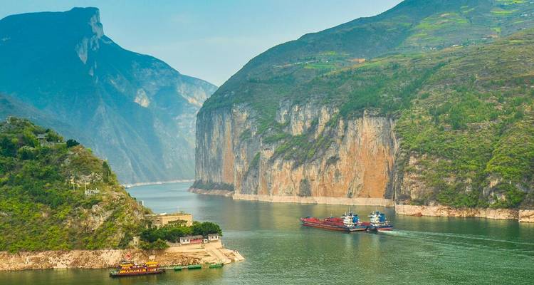 Dramatic green gorge with steep limestone cliffs and cargo boats sailing on the Yangtze River.