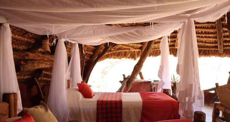 Rustic safari lodge bedroom with draped mosquito nets and thatched roof creating a cozy atmosphere.