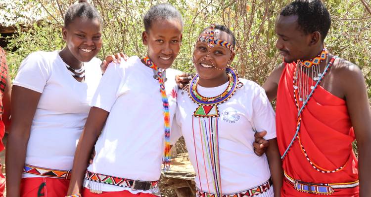 Smiling Maasai women and man wearing traditional beaded jewelry and attire posing together.