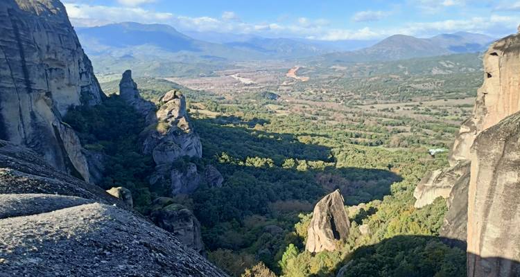 Vue vertigineuse donnant sur les falaises de Météores jusqu'à une vallée en patchwork de champs et de forêts.