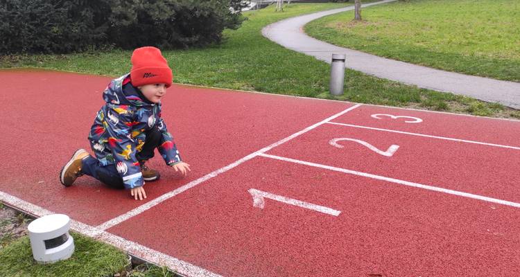Un enfant est agenouillé sur une piste d'athlétisme rouge aux lignes de départ étiquetées 1 2 3.