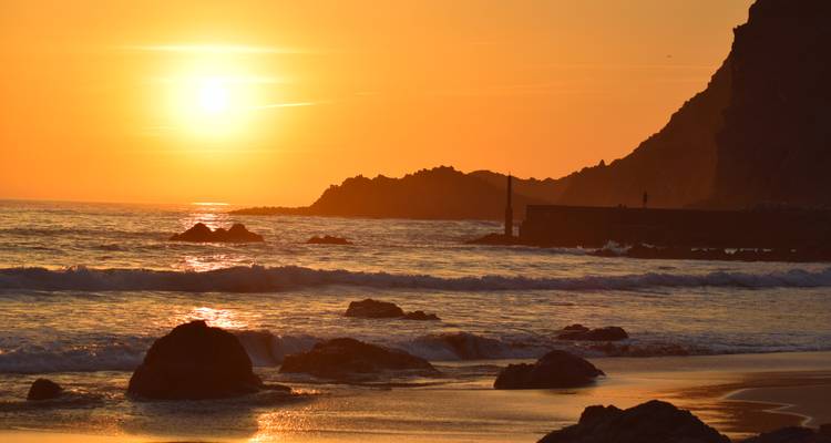 Fiery orange sunset over ocean waves and dark shoreline rocks