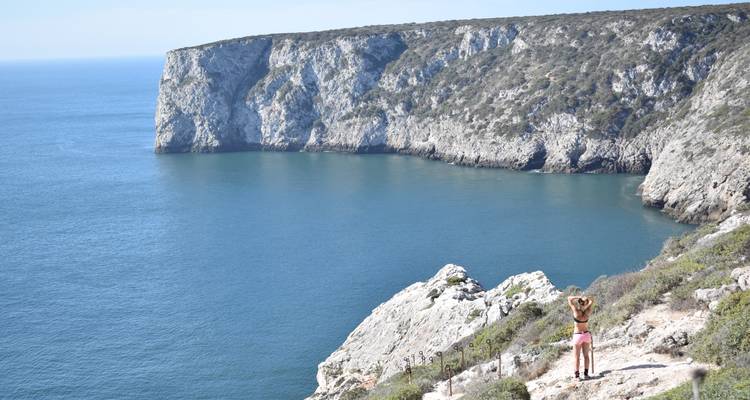 Woman with arms raised enjoying a vast cliff-rimmed bay of deep blue water