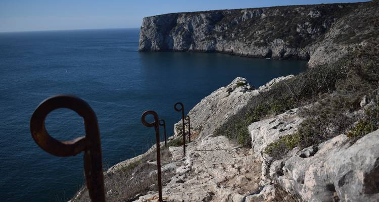 Rocky path with iron rings descending toward dramatic cliffs over deep blue sea