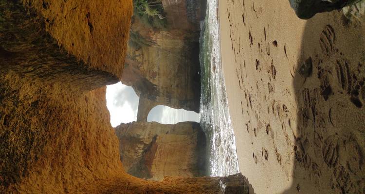 View from inside a sandstone cave framing a distant natural rock bridge over the sea