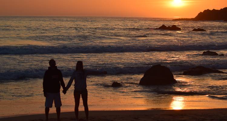 Silhouetted couple holding hands on the beach at vibrant orange sunset