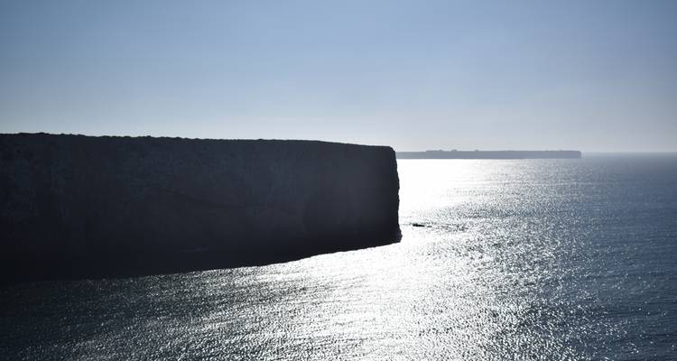 Dramatic dark cliff jutting into a shimmering Atlantic Ocean under bright midday light