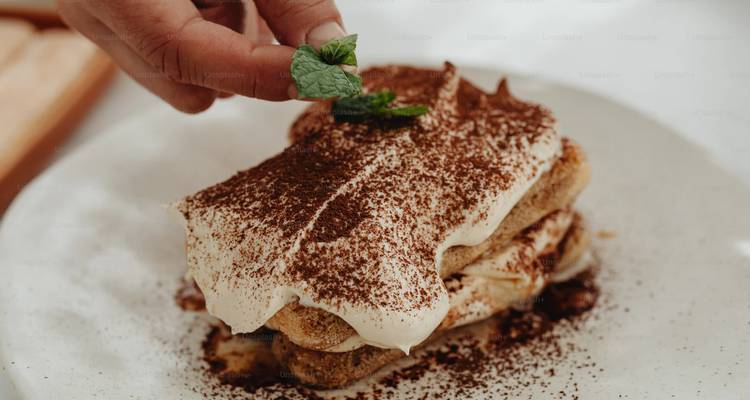 Decorando a mano un plato de tiramisú cremoso espolvoreado con cacao en polvo.
