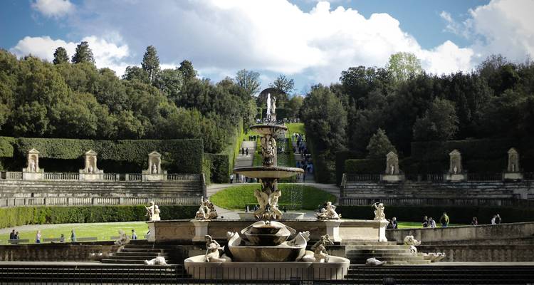 Fuente elegante rodeada de setos bien cuidados y estatuas en un jardín formal.