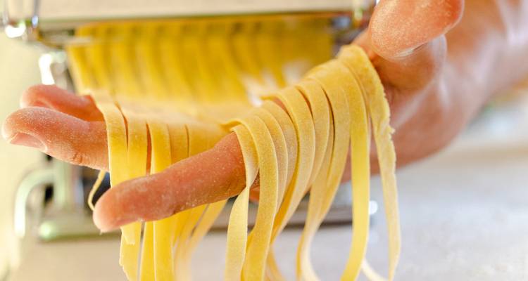 Tiras frescas de pasta colgando de una mano que sale de una máquina para hacer pasta.