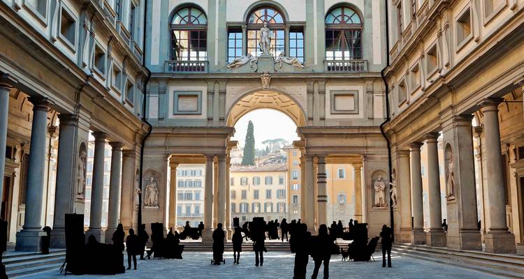 Visitantes en silueta de pie en el gran patio de la Galería de los Uffizi enmarcados por columnas altas.