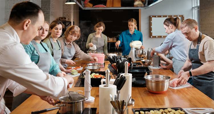 Los participantes de la clase de cocina se reunieron alrededor de una isla de cocina preparando platillos juntos.