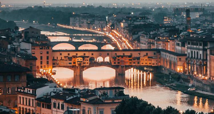 Evening view of the illuminated Ponte Vecchio and its reflections on the Arno River.