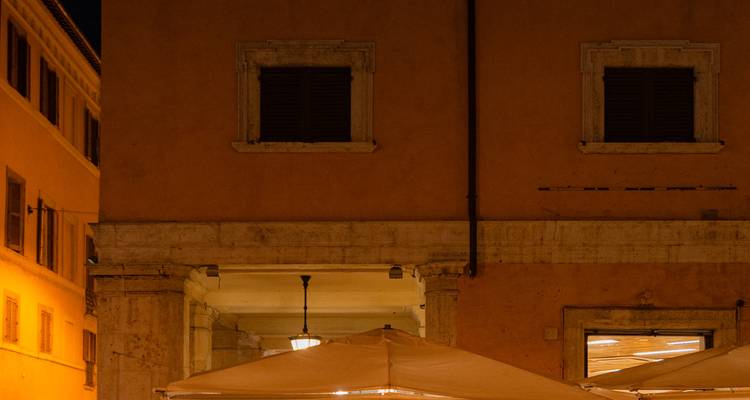 Dimly lit exterior of a rustic building with shuttered windows and covered outdoor seating at night.