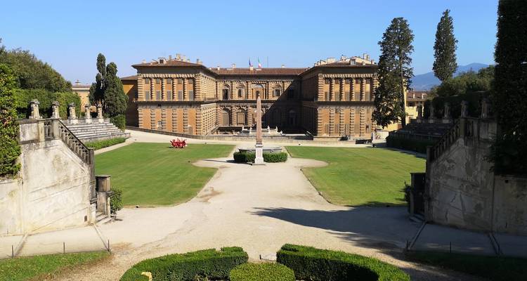 Formal Italian garden leading to the imposing facade of Palazzo Pitti under a clear sky.