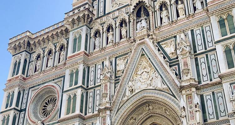 Detailed close-up of the ornate marble facade of Florence’s Duomo against a clear blue sky.