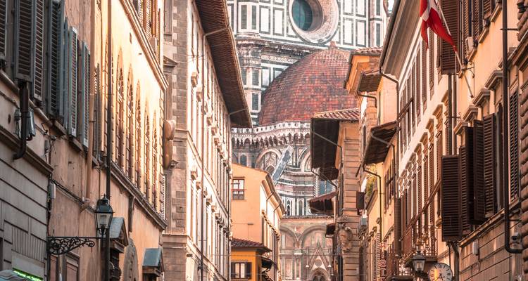 Narrow Florentine street lined with warm-toned buildings leading the eye toward the cathedral dome in the background.