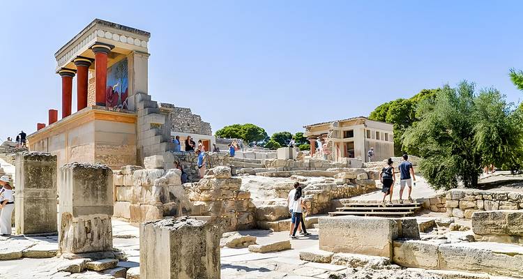 Besucher, die die antiken Ruinen und farbenfrohen rekonstruierten Säulen des Palastes von Knossos an einem sonnigen Tag erkunden.