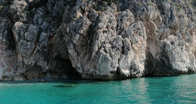 Massive graue Felswand, die sich direkt aus klarem türkisfarbenem Meerwasser erhebt