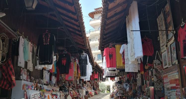 Callejón estrecho en el bazar antiguo de Krujë lleno de artesanías coloridas y ropa tradicional colgando arriba.